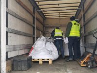Policjant i inspektor WIOŚ kontrolują ciężarówkę. Stoją w naczepie pojazdu przeglądając ładunek.