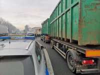 Policyjny radiowóz stoi obok pojazdu ciężarowego. W dali widać kontrolujących kierowcę policjantów.