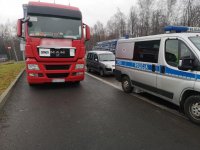 Policyjny radiowóz stoi obok ciężarówki. W radiowozie siedzą policjanci, którzy kontrolują kierowcę.