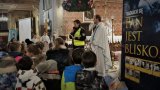 Policjantka razem z księdzem rozmawiają z dziećmi podczas rorat w kościele.
