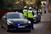 Policjanci stoją przy nieoznakowanym radiowozie.