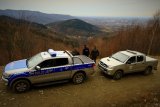 Policjanci i Strażnicy Leśni stoją przy samochodach służbowych, w tle panorama Beskidów.