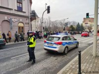 Policjant stoi obok radiowozu zaparkowanego na ulicy.