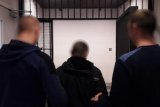 Policjanci wprowadzają podejrzanego o kradzież do celi.