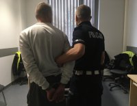 Policjant ruchu drogowego trzyma zatrzymanego nietrzeźwego kierującego.