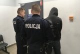 Umundurowani policjanci doprowadzają osobę zatrzymaną.