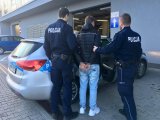 Umundurowani policjanci doprowadzają zatrzymanego do radiowozu.