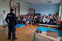 Dzielnicowy prowadzi prelekcję z młodzieżą na sali gimnastycznej.