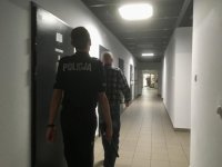 Policjant idzie razem z osadzonym w policyjnym areszcie wzdłuż korytarza.