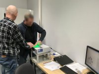 Technik kryminalistyki pobiera zatrzymanemu odciski palców.