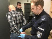 Umundurowany policjant zakłada zatrzymanemu kajdanki.