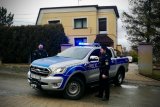 Umundurowani policjanci stoją przy oznakowanym radiowozie.