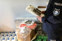 Policjant trzyma w rękach opakowanie z kombinezonem ochronnym.