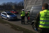 Policjanci i żołnierze WOT stoją przy drodze i obserwują ruch pojazdów.