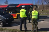 Policjant ruchu drogowego i żołnierz WOT stoją przy drodze, na drugim planie kolejny policjant i autobus miejski.
