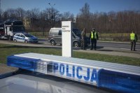 Dach policyjnego radiowozu, w tle pojazdy zatrzymywane do kontroli przez policjantów.