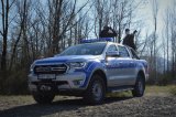 Umundurowany policjant i funkcjonariusz Straży Rybackiej stoją nad rzeką. Obok oznakowany policyjny wóz Ford Ranger.