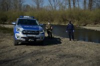 Umundurowany policjant i funkcjonariusz Straży Rybackiej stoją nad rzeką. Obok oznakowany policyjny wóz Ford Ranger.