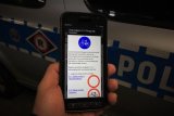 widok telefonu trzymanego w ręce.W tle widać policyjny radiowóz.