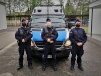 Policjanci z bielskiego pododdziału prewencji stoją przed radiowozem. Mundurowi mają zasłonięte twarze maseczkami.