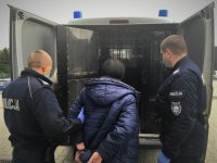 Umundurowani policjanci wprowadzają zatrzymaną kobietę do policyjnego radiowozu.