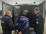 Umundurowani policjanci wprowadzają zatrzymaną kobietę do policyjnego radiowozu.
