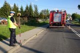 Policjant ruchu drogowego mierzy miejsce wypadku. W tle wóz straży pożarnej.