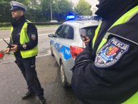Policjanci stoją przy radiowozie. Na pierwszym planie naszywka policyjnego munduru.