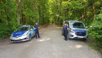 Policjant i Strażnik Miejski stoją przy radiowozie na wjeździe do lasu.