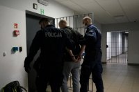 Umundurowani policjanci doprowadzają zatrzymanego.