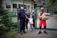 Policjant stoi przed domem dziecka w towarzystwie jednej z podopiecznych, wychowawców i ratownika medycznego.