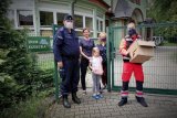 Policjant stoi przed domem dziecka w towarzystwie jednej z podopiecznych, wychowawców i ratownika medycznego.