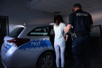 Policjant doprowadza zatrzymaną kobietę do radiowozu