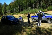 Policjanci kontrolują SUV-a na leśnej drodze. Policjant jeżdżący motocyklem stoi w kasku.