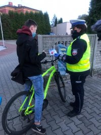 Policjantka rozmawia z rowerzystą i przekazuje mu lampkę rowerową.