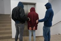 Nieumundurowani policjanci stoją z zatrzymaną przed windą.