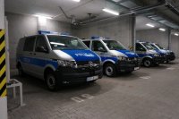 Cztery radiowozy policyjne oznakowane marki Volkswagen T6 stoją zaparkowane na podziemnym parkingu.