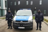 Umundurowani policjanci stoją po obydwu stronach radiowozu oznakowanego marki VW T6