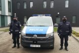 Umundurowani policjanci stoją po obydwu stronach radiowozu oznakowanego marki VW T6