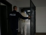 Umundurowany policjant wprowadza zatrzymanego przez otwartą kratę do pomieszczeń