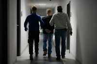 Nieumundurowani policjanci doprowadzają zatrzymanego poszukiwanego Europejskim Nakazem Aresztowania.