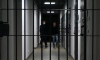 Widok przez kratę aresztu. Na drugim planie widać umundurowanego policjanta i osobę zatrzymaną.