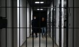 Widok przez kratę aresztu. Na drugim planie widać umundurowanego policjanta i osobę zatrzymaną.