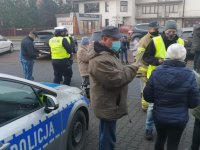 Mężczyzna stoi obok radiowozu, w tle policjanci w kamizelkach odblaskowych.