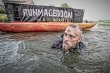 Mężczyzna płynie w wodzie zanurzony po szyje, w tle logotyp biegu Runmageddon