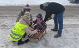 Pracownica Wojewódzkiego Ośrodka Ruchu Drogowego w Bielsku-Białej przekazuje opaskę odblaskową dziecku na saneczkach.