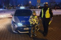 Policjantka ruchu drogowego stoi z dzieckiem przed radiowozem.