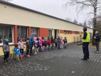 Policjant prowadzi prelekcję dla przedszkolaków przed budynkiem przedszkola.
