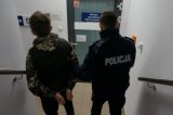 Umundurowani policjanci prowadzą podejrzanego klatką schodową komendy.