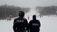 Dwaj umundurowani policjanci stoją tyłem do zdjęcia i obserwują stok narciarski.